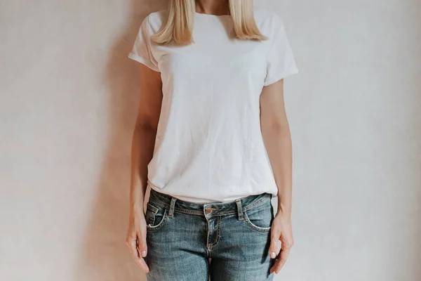 Blond hair woman posing near a light wall. Beautiful young caucasian girl. Hand gestures. Emotion. Casual clothing. Studio model in work. Strong woman, future is female. Jeans and white blank t-shirt