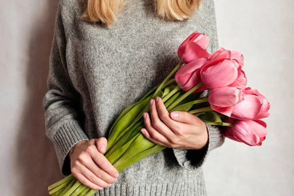 Happy woman holds tulips in her hands. Florist girl gathered a bouquet. Beautiful pink flowers. Blossom petal. Gift for the holiday celebration, springtime mood. Romantic surprise from a loved one