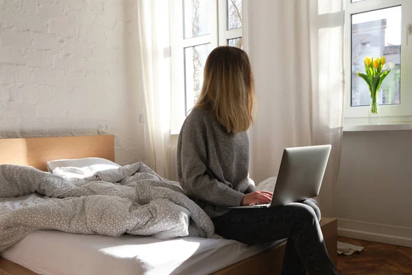Kadın dizüstü bilgisayarı elinde tutuyor. Evde sabah online aktiviteleri. Yatakta rahatla, bilgisayarda film ve TV şovları izle. Sosyal medya bağımlılığı. Evde çalışıyor, serbest çalışıyor. Yaşam tarzında teknoloji