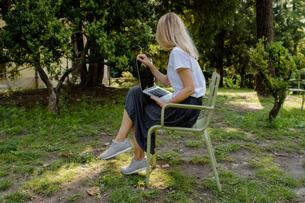 Bir kadın dizüstü bilgisayarda klavye kullanıyor. Çevrimiçi iş açık havada. Parkta serbest çalışan bir kız. Çalışma alanı. Modern iş günü. Uzaktan kumanda. Yaşam tarzı. Mobil cihaz. Dizüstü bilgisayarın kapatma düğmeleri