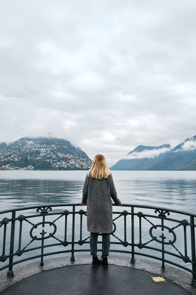 Güzel beyaz kadın Lugano 'da iskelede duruyor. Seyahat eden bir kız. Lugano Gölü, Alplerin güney yamacı. İsviçre 'de manzara. İnanılmaz manzaralı açık hava manzarası. Ticino Kantonu. Macera yaşam tarzı