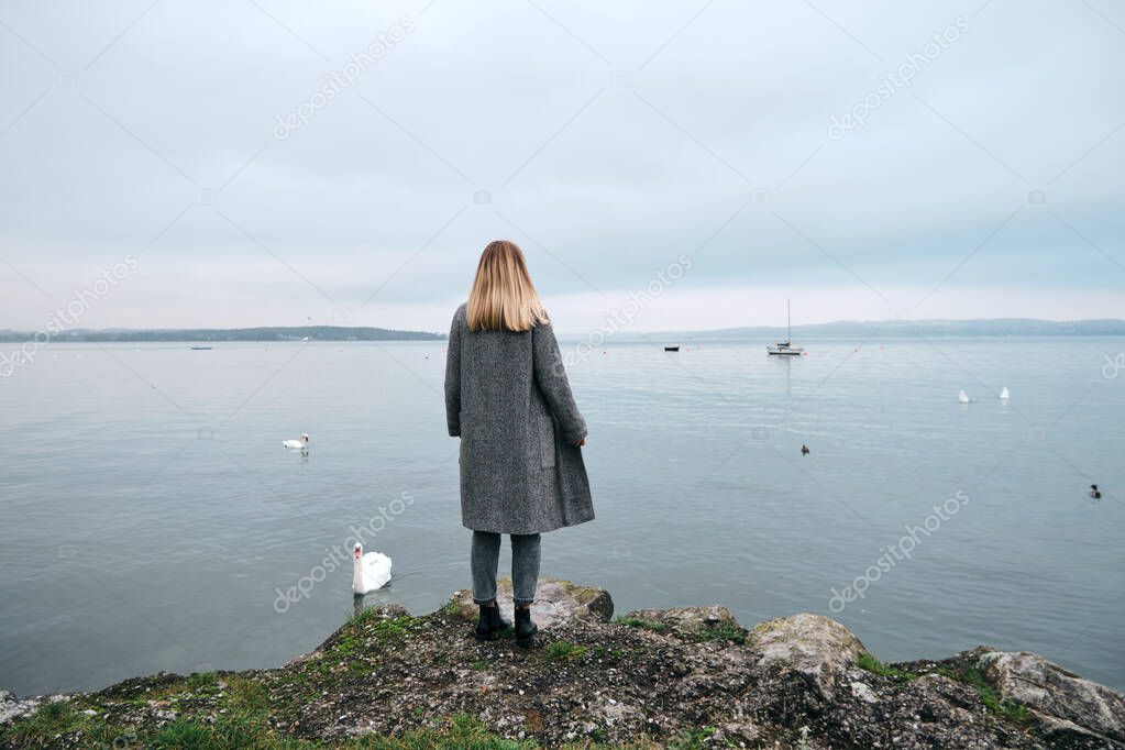 Beautiful blond hair woman enjoy panorama by the Bodensee lake. Landscape in Switzerland. Happy girl in travel. Amazing scenic outdoors view. Dramatic sky. Swans on water. Adventure lifestyle, freedom