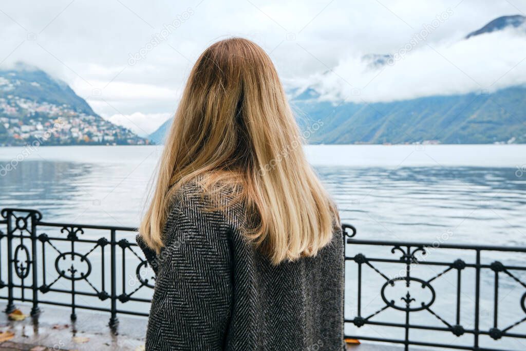 Beautiful caucasian woman stands on pier in Lugano. Girl in travel. Lake Lugano, southern slope of Alps. Landscape in Switzerland. Amazing scenic outdoors view. Canton of Ticino. Adventure lifestyle