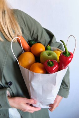 Trençkotlu bir kadın ve bir paket taze sebze ve meyve. Sağlıklı beslenme, biyoorganik gıdalar. Marketten alışveriş yapmak. Kadın diyeti. Vejetaryen yaşam tarzı. Yemek pişirmeye hazır.
