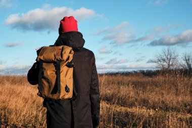 Açık arazide yürüyen bir adam. Güzel sonbahar manzarası, sonbahar yaprakları. Kırsal manzaralı günbatımı. Hafta sonu dinlenip dinlenin. Sırt çantalı şık bir adam. Akşam macerası