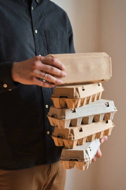 Tavuk yumurtalı karton kutular. Bir adam pişmemiş yumurtalarla dolu kutuları tutar. Doğal organik tarım ürünü. Paskalya tatiline hazırlanıyorum. Taze yemek teslimatı, karton paket. Yemek pişirmek için ham malzeme.