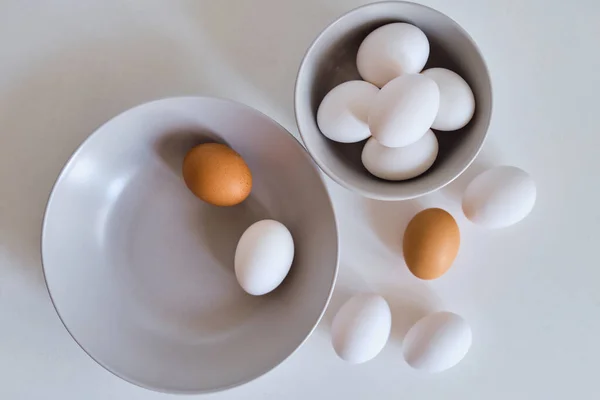 Chicken eggs on minimalist plates. Art photo with uncooked eggs on white table. Natural organic farm product. Preparing for Easter holiday. Kitchen art, dish on cuisine. Raw ingredient for cooking eat