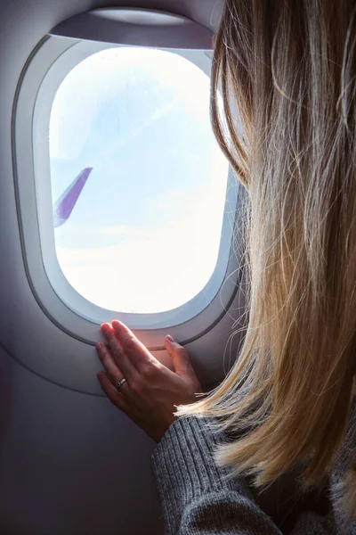 Kadın uçağın penceresinden dışarı bakıyor. Elini pencerenin yanına koy. Uçaktaki kız. Uçak kanadı, manzara manzarası. Güzel bulut, mavi gökyüzü. Uçakla seyahat, macera. Hava ulaşımı. Havacılık