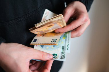 Adam parayı elinde tutuyor. Ödeme ya da takas için euro olarak nakit. Erkek, euro banknotlarında maaşı sayar. Para biriktirmek, banka depozitosu çekmek. Avrupa parası. Finansal kriz. Eller yakın plan.