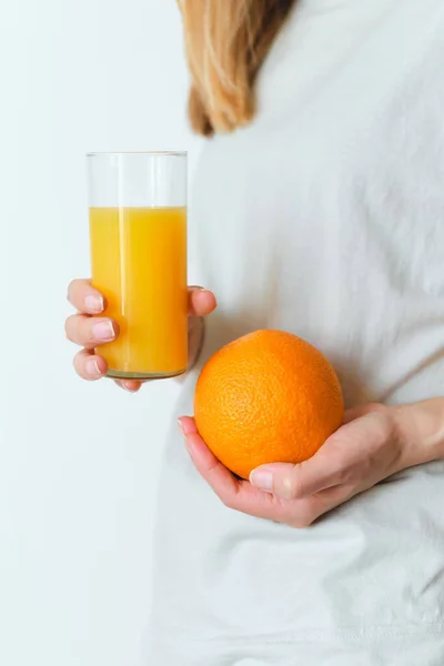 Girl holds a glass of orange juice in her hands. Fresh natural orange juice. Vitamin drink for breakfast. Healthy lifestyle, organic diet. Refreshment after morning fitness. Enjoy delicious beverage