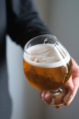 Bir adamın elinde bir bardak bira var. Bira tatmak için. Güzel köpüklü bira. Soğuk içecek içeceği. Bardan alkollü içecek. Bira degulasyonunda rahatlama ve keyif 
