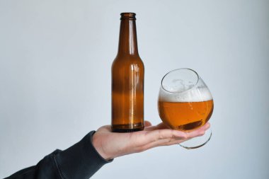 Bir adamın elinde bir bardak bira ve şişe. Bira tatmak için. Güzel köpüklü bira. Soğuk içecek içeceği. Alkol içeceği. Bira degulasyonunda rahatlama ve keyif