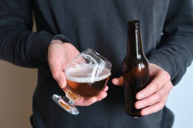 Bir adamın elinde bir bardak bira ve şişe. Bira tatmak için. Güzel köpüklü bira. Soğuk içecek içeceği. Alkol içeceği. Bira degulasyonunda rahatlama ve keyif