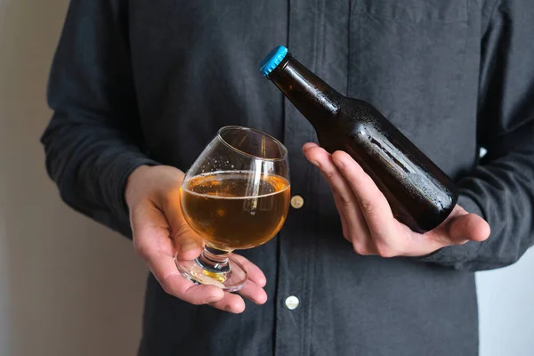 A glass of beer and bottle in the hands of a man. Tasting brewed craft beer. Lager beer with beautiful foam. Cold refreshment beverage. Alcohol drink. Relaxation and enjoyment on beer degustation