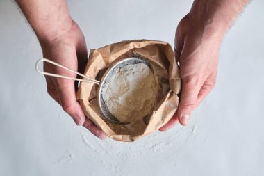 Adam elinde bir torba un tutuyor. Un eleği. Hamuru pişirmek için hazırlıyorum. Aile için ev yapımı yemek yapmak. Şef mutfakta hamur işi pişiriyor. Sağlıklı, lezzetli yemek tarifi.