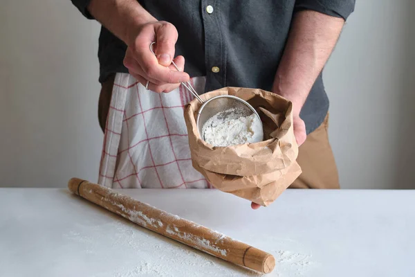 Man holds a bag of flour in his hands. Flour sieve and rolling-pin. Preparing the dough for baking. Making homemade cuisine for family. Chef in the kitchen cooking pastry. Healthy delicious culinary