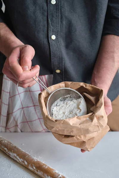 Man holds a bag of flour in his hands. Flour sieve and rolling-pin. Preparing the dough for baking. Making homemade cuisine for family. Chef in the kitchen cooking pastry. Healthy delicious culinary