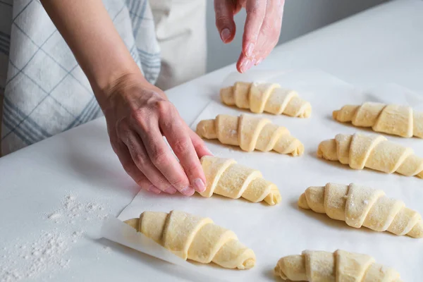 A woman is cooking croissants. Prepare for baking. Delicious traditional french crispy croissants for breakfast. Homemade bakery, cuisine for family. Girl chef work on kitchen table. Raw croissants