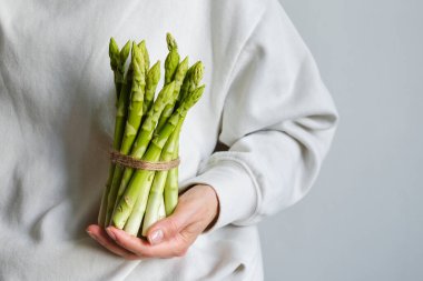 Bir kızın ellerinde yeşil kuşkonmaz. Bir sürü taze kuşkonmaz. Sağlıklı organik yiyecekler. Evde yemek pişirmek. Doğal vitaminler, yemek için ham malzeme. Özenle seçilmiş biyolojik kuşkonmaz.