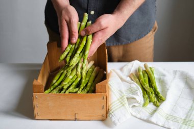 Bir adamın ellerinde yeşil kuşkonmaz. Bir sürü taze kuşkonmaz. Sağlıklı organik yiyecekler. Evde yemek pişirmek. Doğal vitaminler, yemek için ham malzeme. Özenle seçilmiş biyolojik kuşkonmaz.