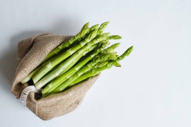 Çuvalda yeşil kuşkonmaz. Torba ve sicim. Bir demet taze kuşkonmaz. Sağlıklı organik yiyecekler. Evde yemek pişirmek. Doğal vitaminler, yemek için ham malzeme. Özenle seçilmiş biyolojik kuşkonmaz.