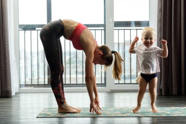 Genç anne evde bebeğiyle yoga yapıyor.