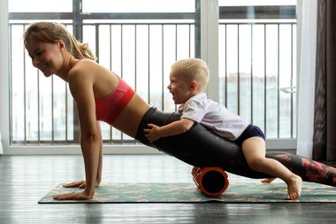 Genç anne evde bebeğiyle yoga yapıyor.