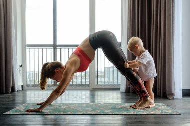 Genç anne evde bebeğiyle yoga yapıyor.