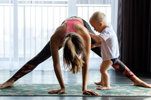 Genç anne evde bebeğiyle yoga yapıyor.