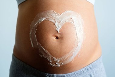 Müstakbel anne çıplak göbeğine sürdüğü nemlendirici kremden yapılmış kalp işareti ile poz veriyor. Hamilelik boyunca cilt bakımı nemlendirici ve besin.