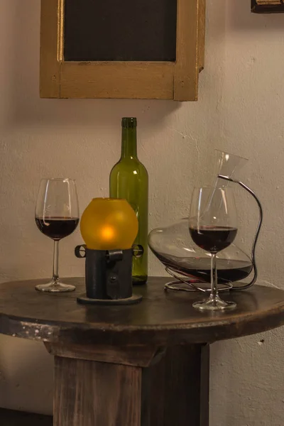 Red wine glass in front of an empty green bottle and crystal wine container with old lamp over dark wood table — Stock Photo, Image