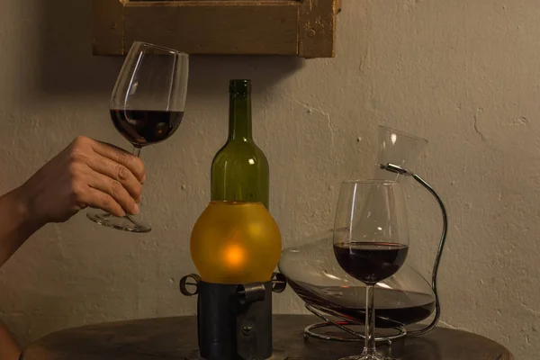 Ahşap bir masanın üzerinde şarap kadehini tutan kadın, şarap kabı ve eski bir lamba.
