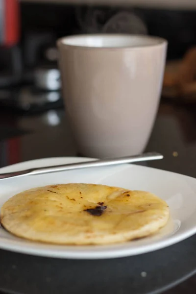 Arepa colombiana en un plato blanco y una taza de café en el fondo — Foto de Stock