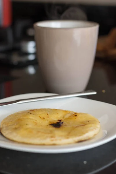 Beyaz bir tabakta Kolombiya arepası ve arka planda bir fincan kahve.
