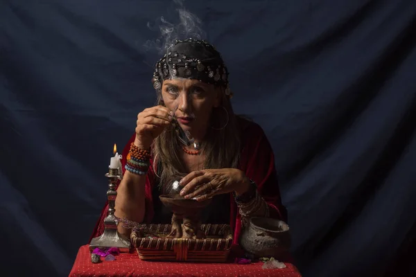 Çingene falcı ya da gizemli kahin elinde dumanı tüten bir odun parçası ve sihirli bir kristal küre tutuyor.