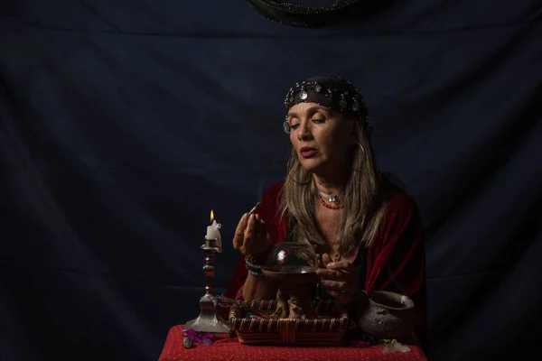 Çingene falcı ya da gizemli kahin elinde dumanı tüten bir odun parçası ve sihirli bir kristal küre tutuyor.