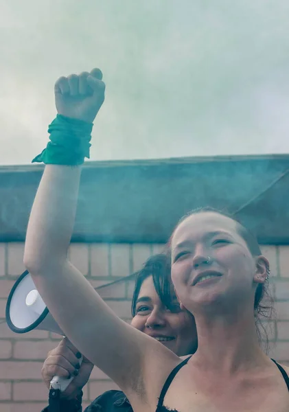 Young feminist activists with fist rised and megaphone loudspeakers surrounded by green smoke
