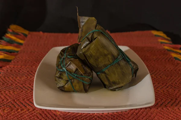 Colombian tamales on a white plate and a traditional red fabric