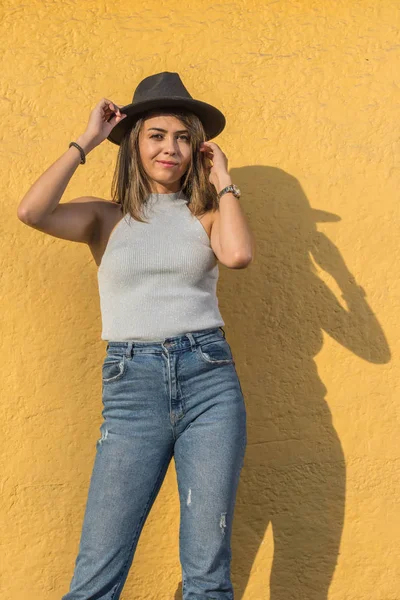 Genç ve güzel bir Latin kadının portresi. Siyahını alıyor ve sarı duvarda saçlarına dokunuyor.