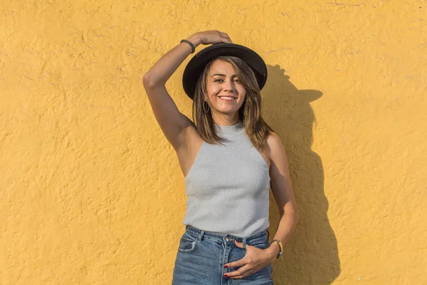 Genç ve güzel bir Latin kadının portresi gülümsüyor. Siyah şapkasını sarı duvara asıyor.