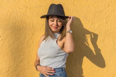 Siyah şapkasını alıp sarı duvara bakan güzel Latin bir kadının portresi.