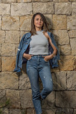 Güzel seksi Latin kadın eski duvar taşına yaslanmış kot ceketle poz veriyor.