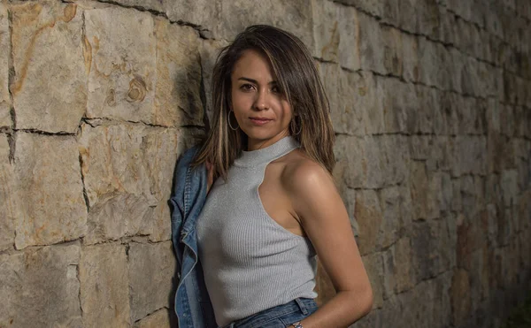 Genç Latin bir kadın şehirde dolanıyor, taş duvara yaslanıyor. Moda konsepti