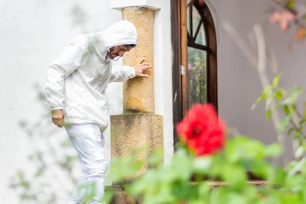 Kapüşonlu beyaz giysili bir adam Hıristiyan kilisesinin kapısına dayanıyor.