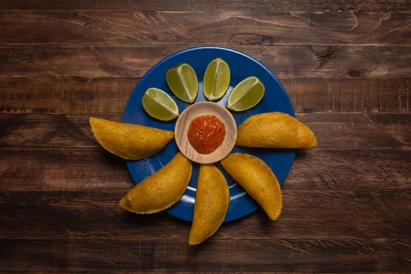Mavi tabakta limon ve baharat soslu tipik Kolombiya böreği ve koyu ahşap arka plan.