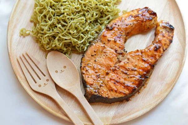 Grilled salmon and green noodle with smiley wooden spoon and for