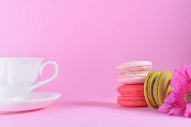 French colourful macarons with happy cup on pink pastel background. Romantic concept with copy space for design works. Sweet dessert for tea time or coffee break.Concept about love and relationship
