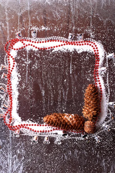Рамка снега с еловыми конусами и рождественские бусины на темном деревянном фоне снежный зимний буклет — стоковое фото
