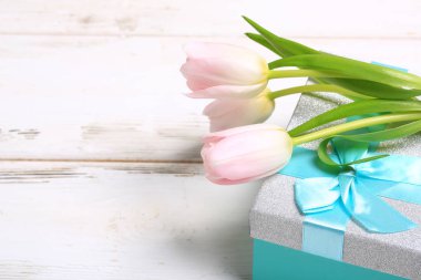 Beyaz ahşap bir masada hediye kutusunda pembe laleler.