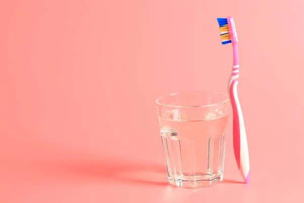 Escova de dentes e um copo de água em um fundo rosa — Fotografia de Stock